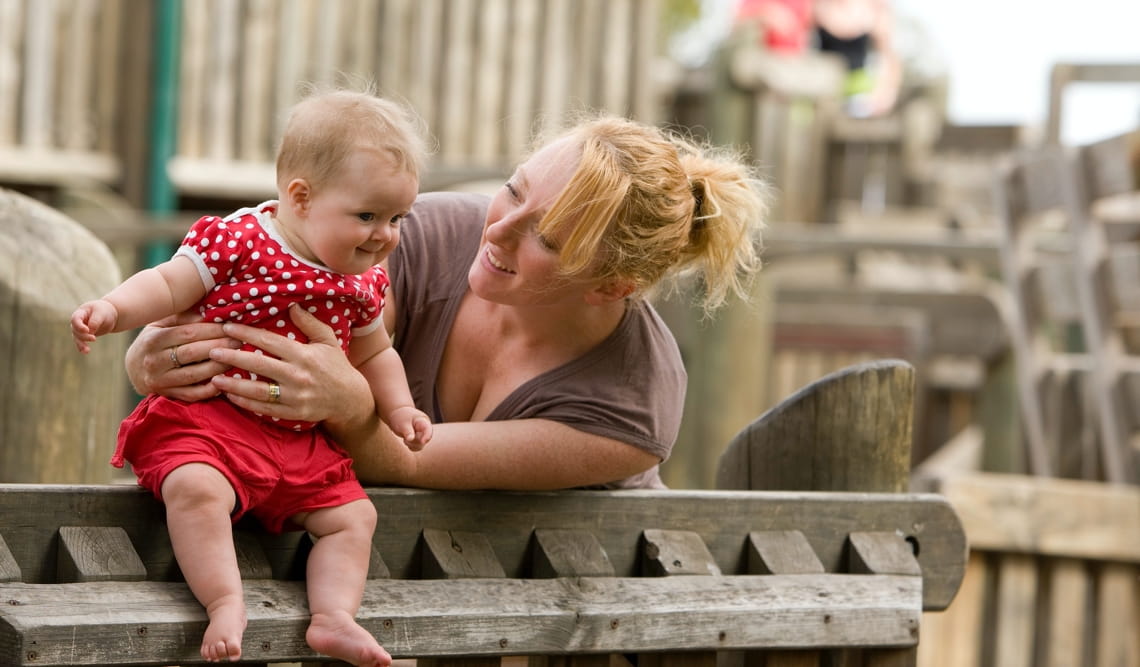A mother holds her baby on the railing of a wooden playground in Albert Park. 