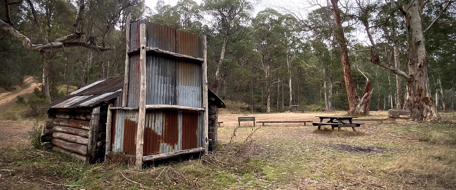 View of a hut and picnic table and bench in a camping area.