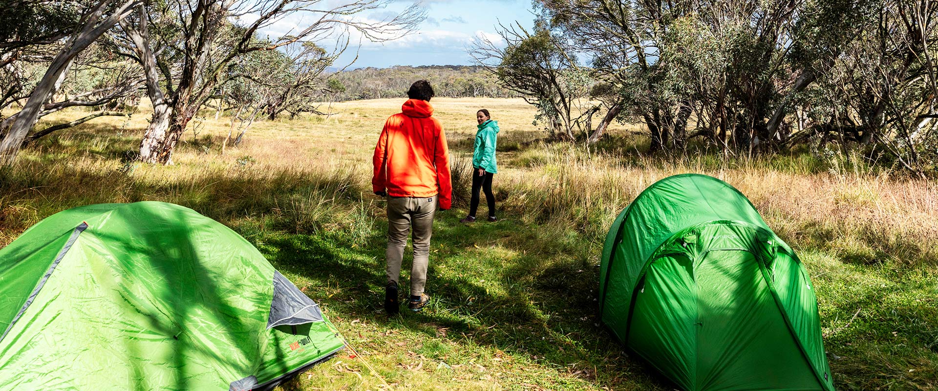 Two hikers walk past their tents out towards an open plain 