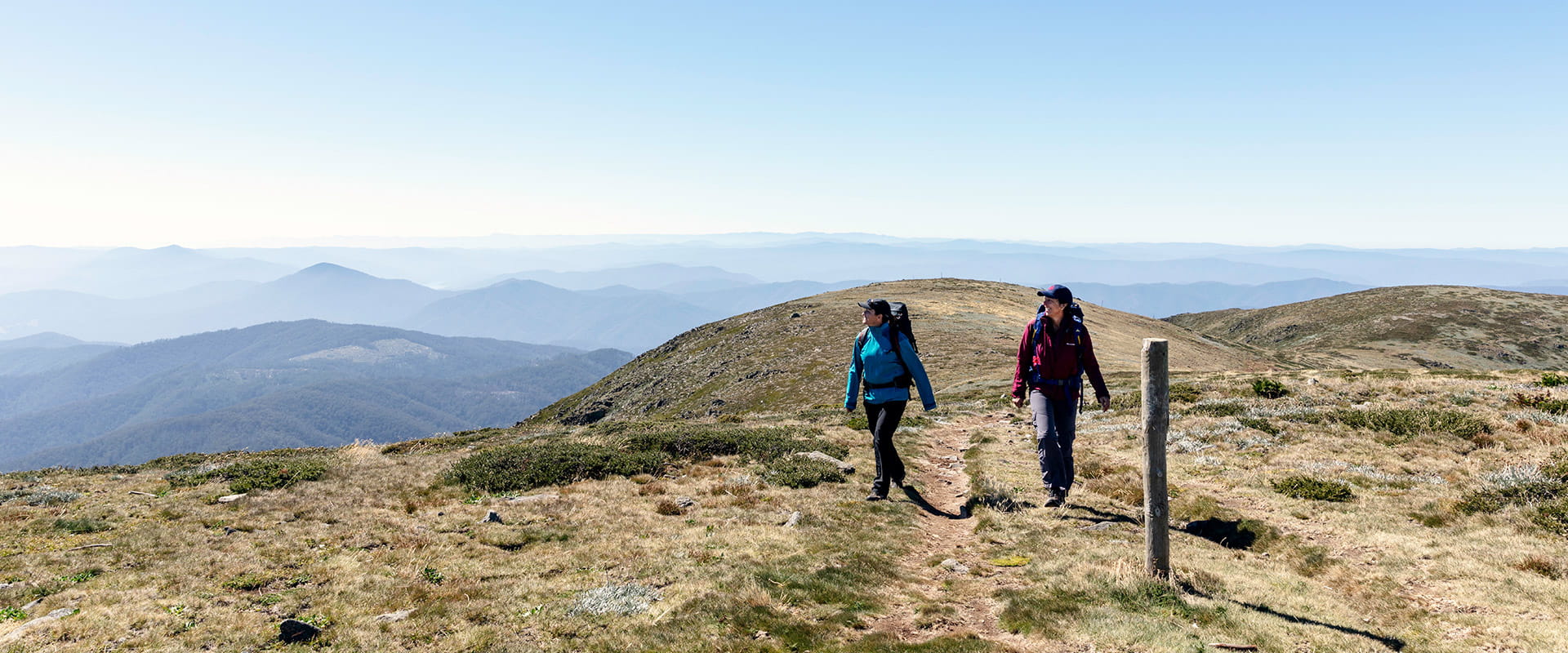 Two hikers walk towards the summit, surrounded by breathtaking mountain view 
