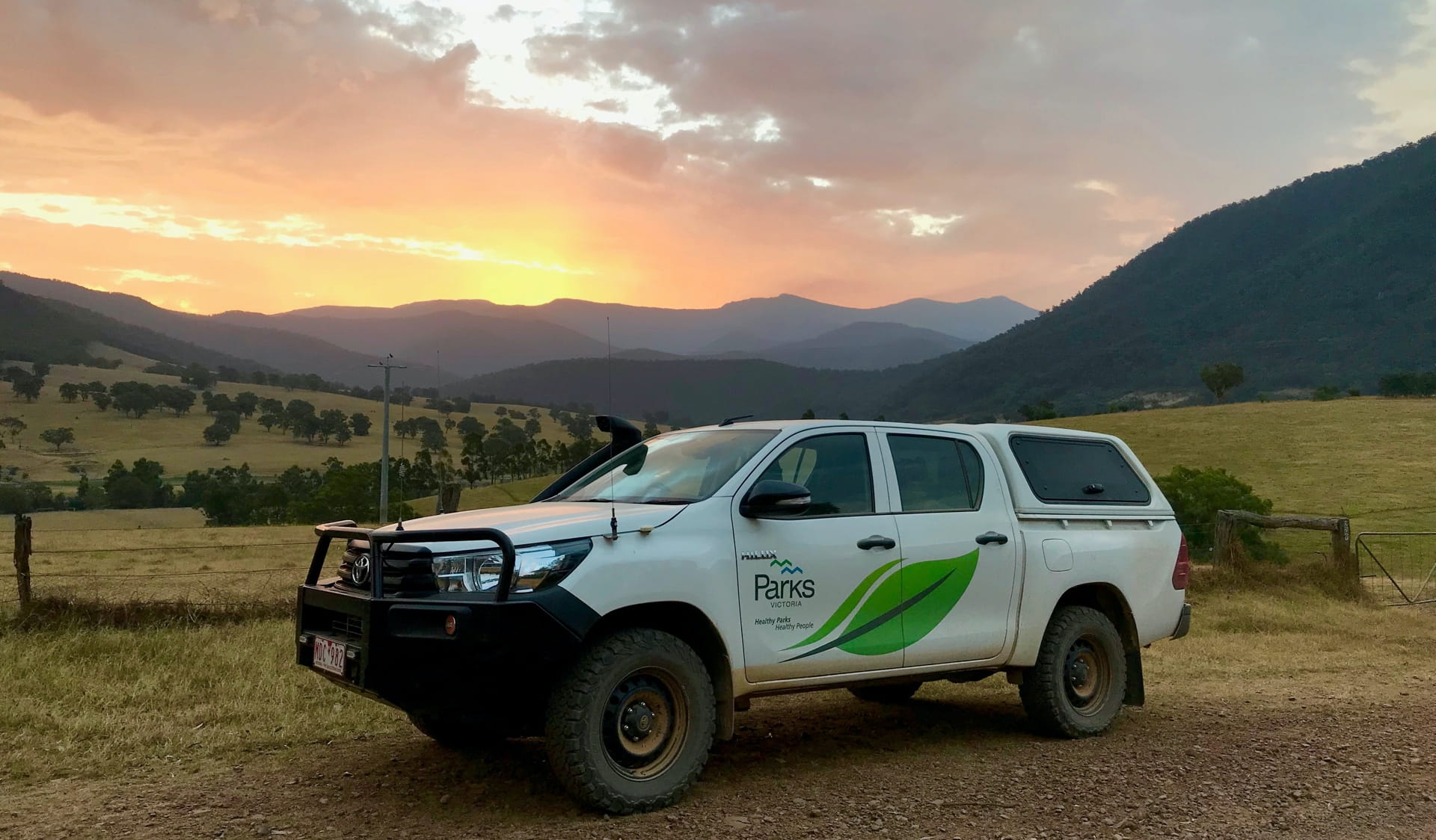 A Parks Victoria 4WD parked in front of a sunset over the mountains in Alpine National Park