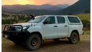 A Four Wheel Drive sits on a dirt track with a sunset highlighting the mountains in the background.