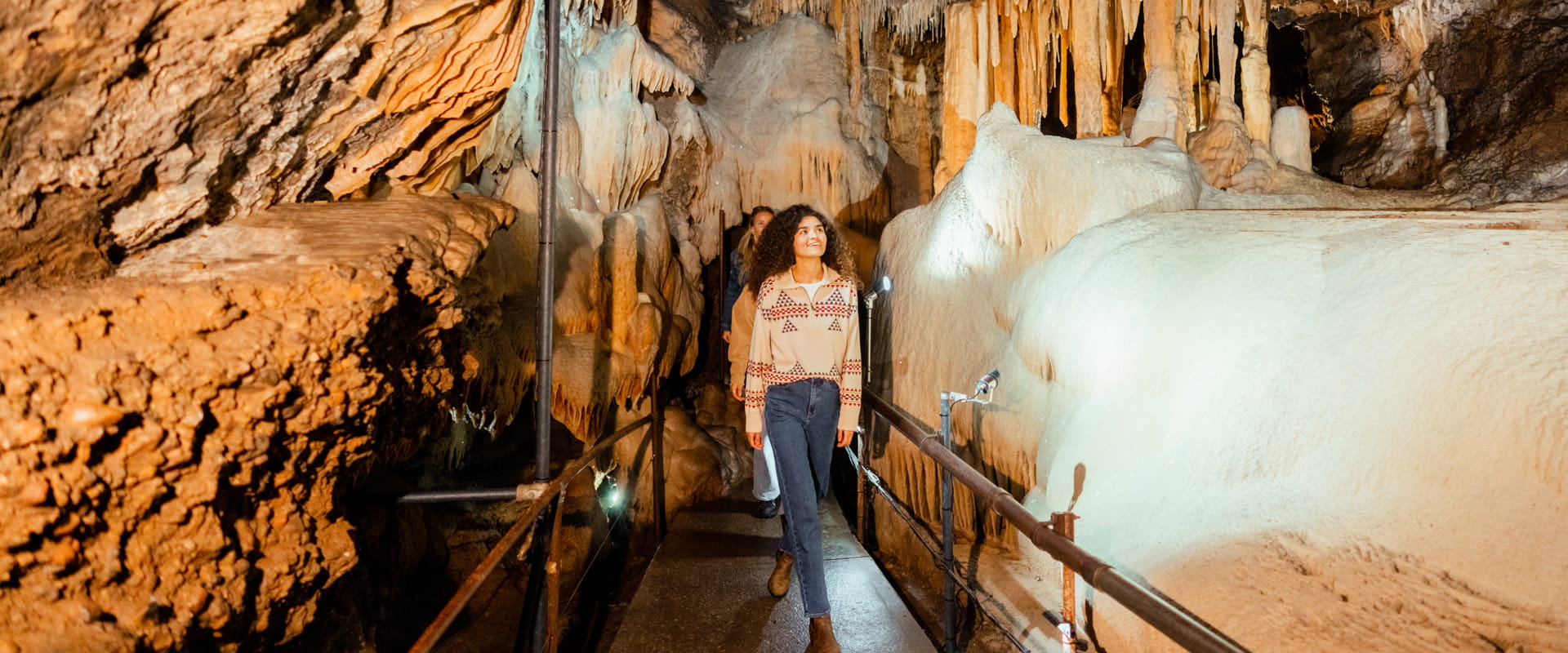 A young woman looking up to admire the surrounding limestone stalactite formations inside a cave.