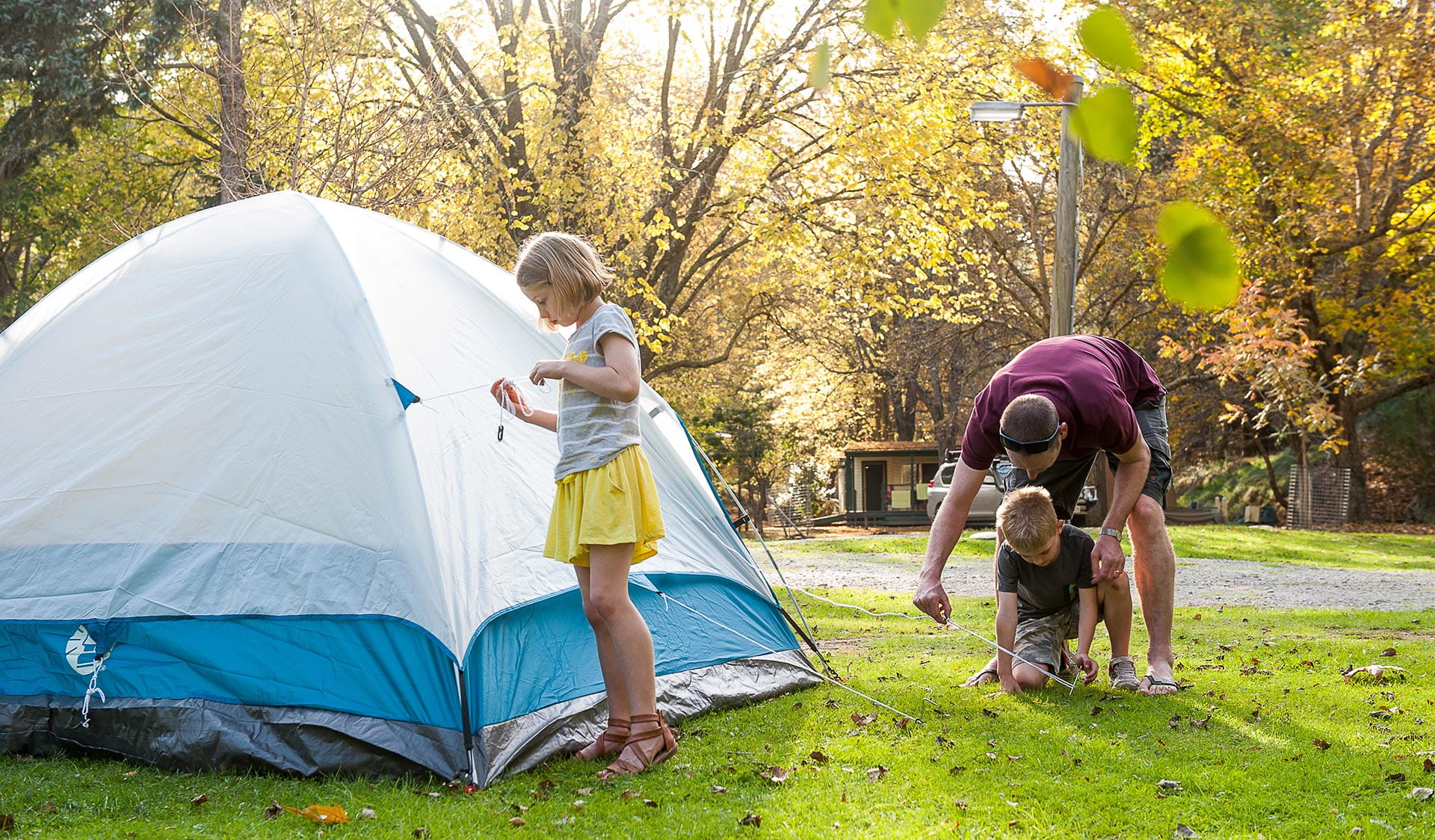 A man with two children next to their tent on grass.