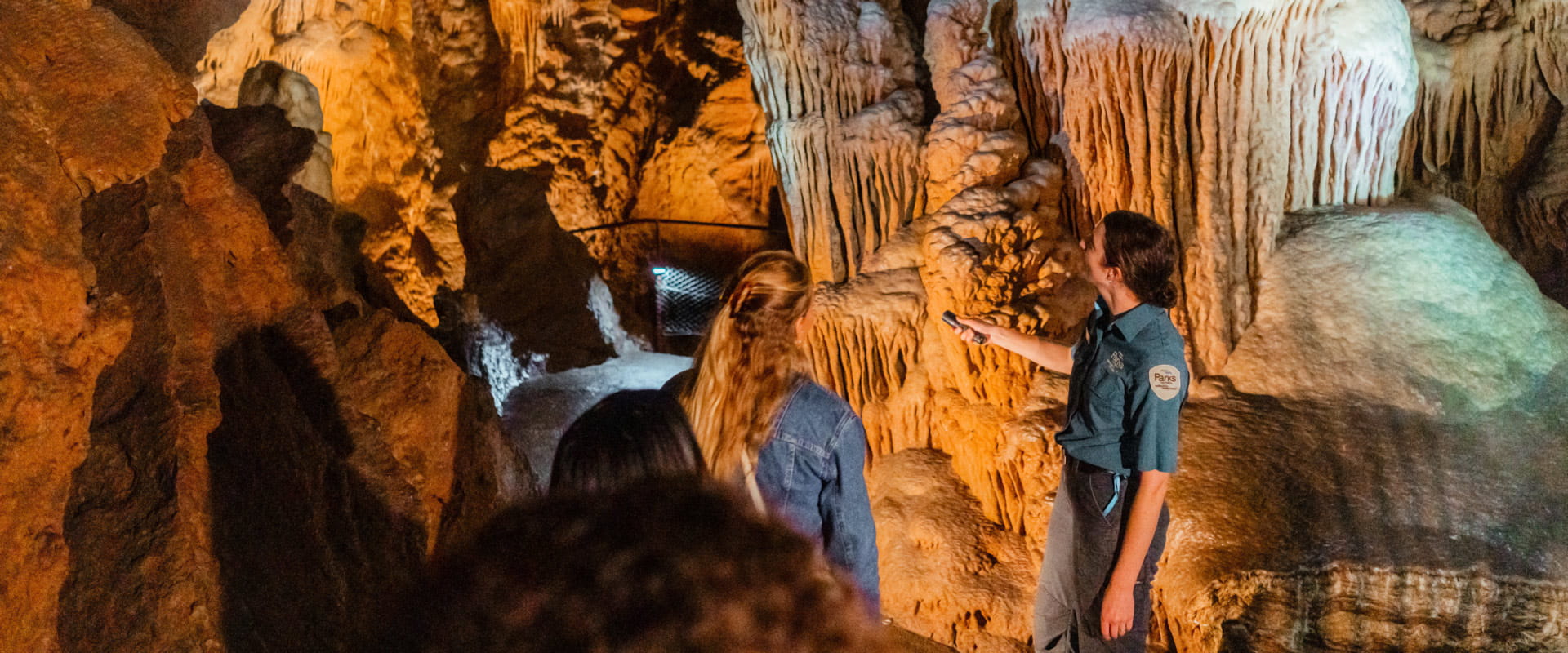 A park ranger shines a small torchlight onto the grand limestone formations during a cave tour.