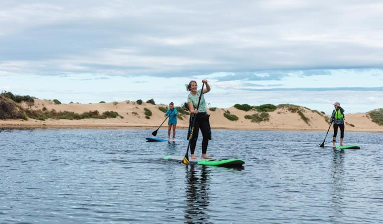 Three women stand-up paddle boarders paddle up the Yeerung River.