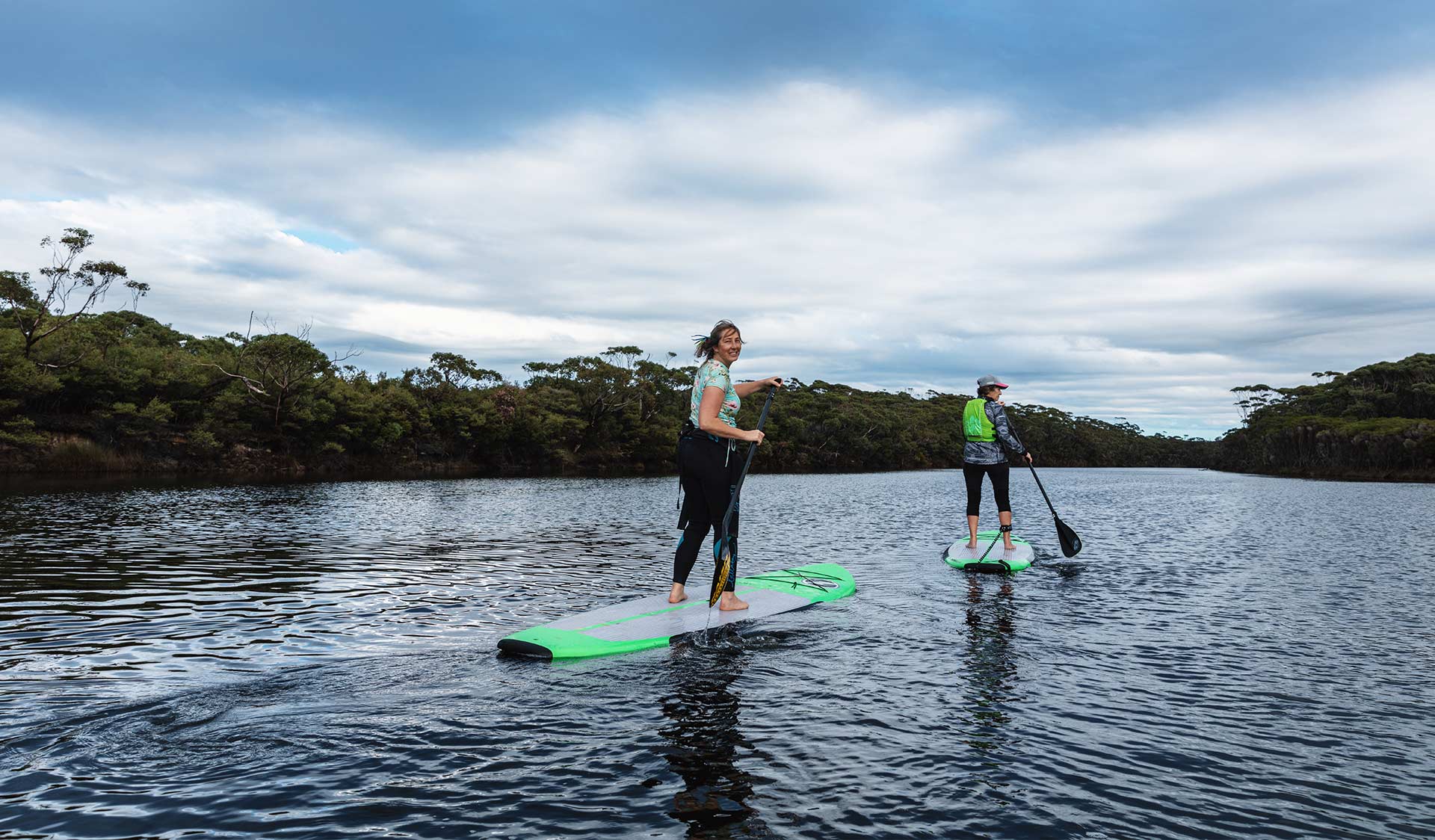 Two women stand-up paddle boarders paddle up the Yeerung River.
