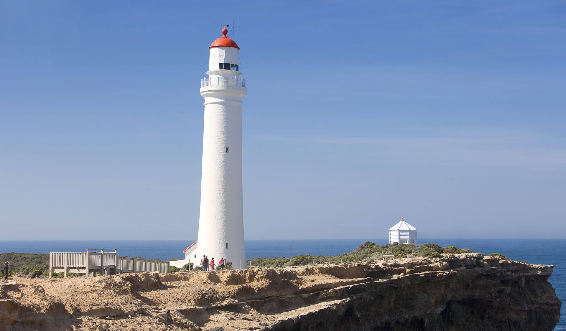 A tall white lighthouse on a rocky coastline.