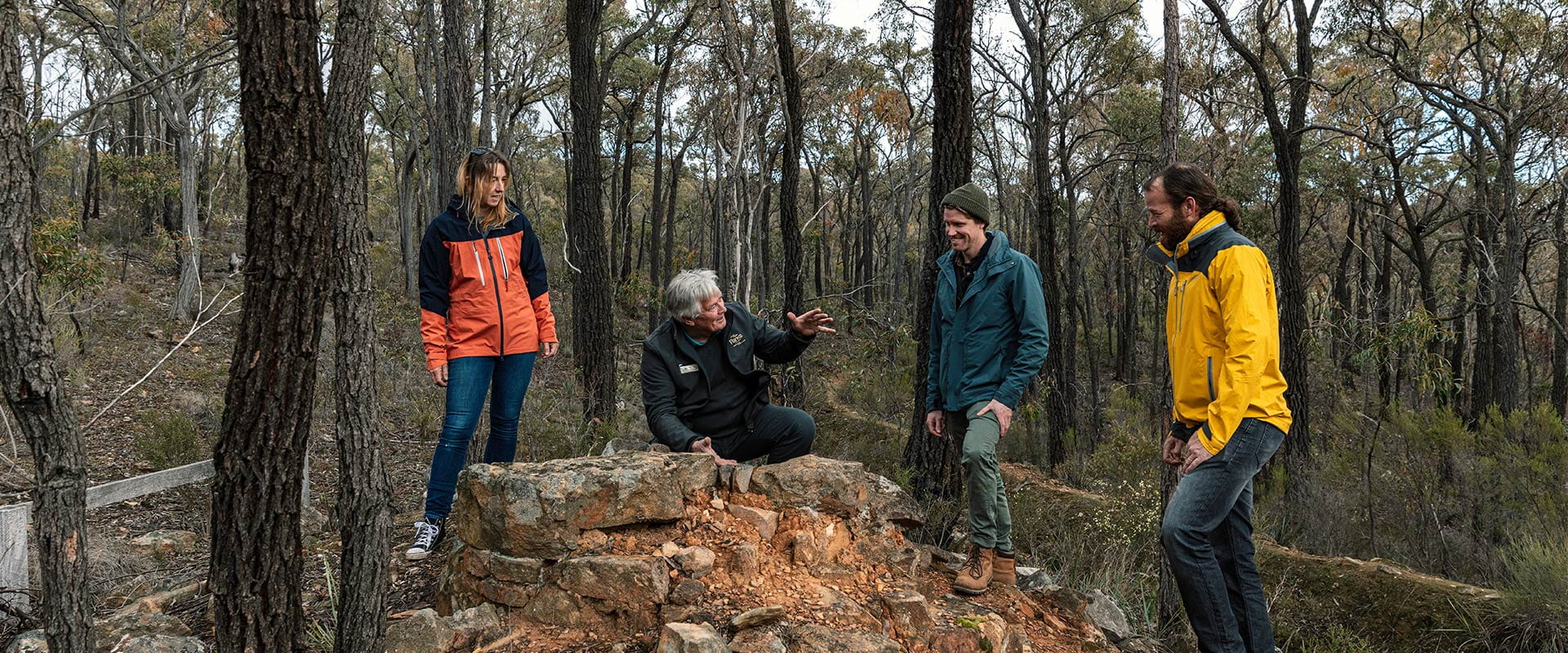 A group of people discuss the significance of a small cluster of stonework amongst a rugged bushland