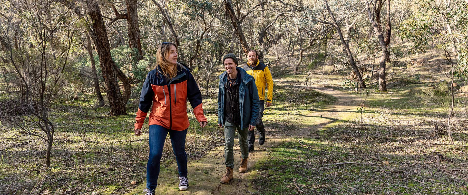 A small group of hikers walk along a dirt trail amongst rugged bushland