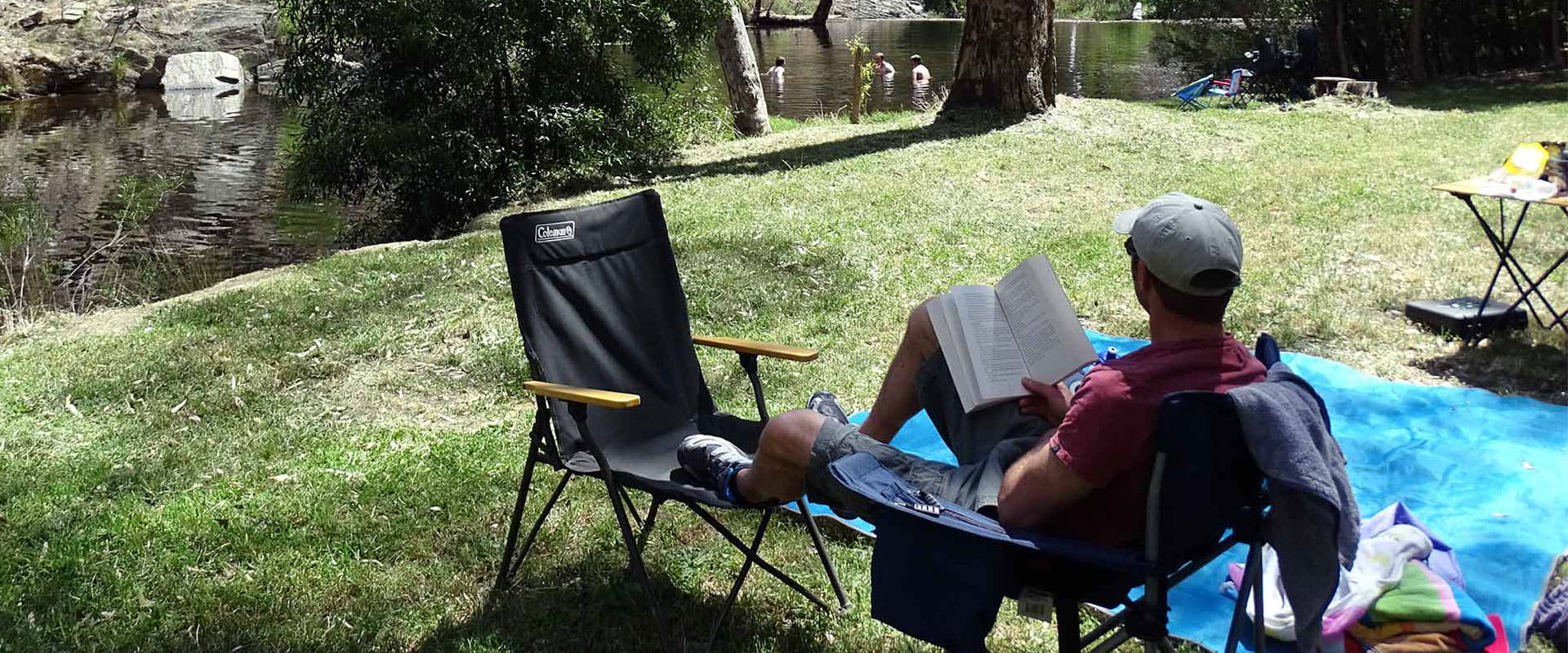 A man relaxes in a camping chair reading a book