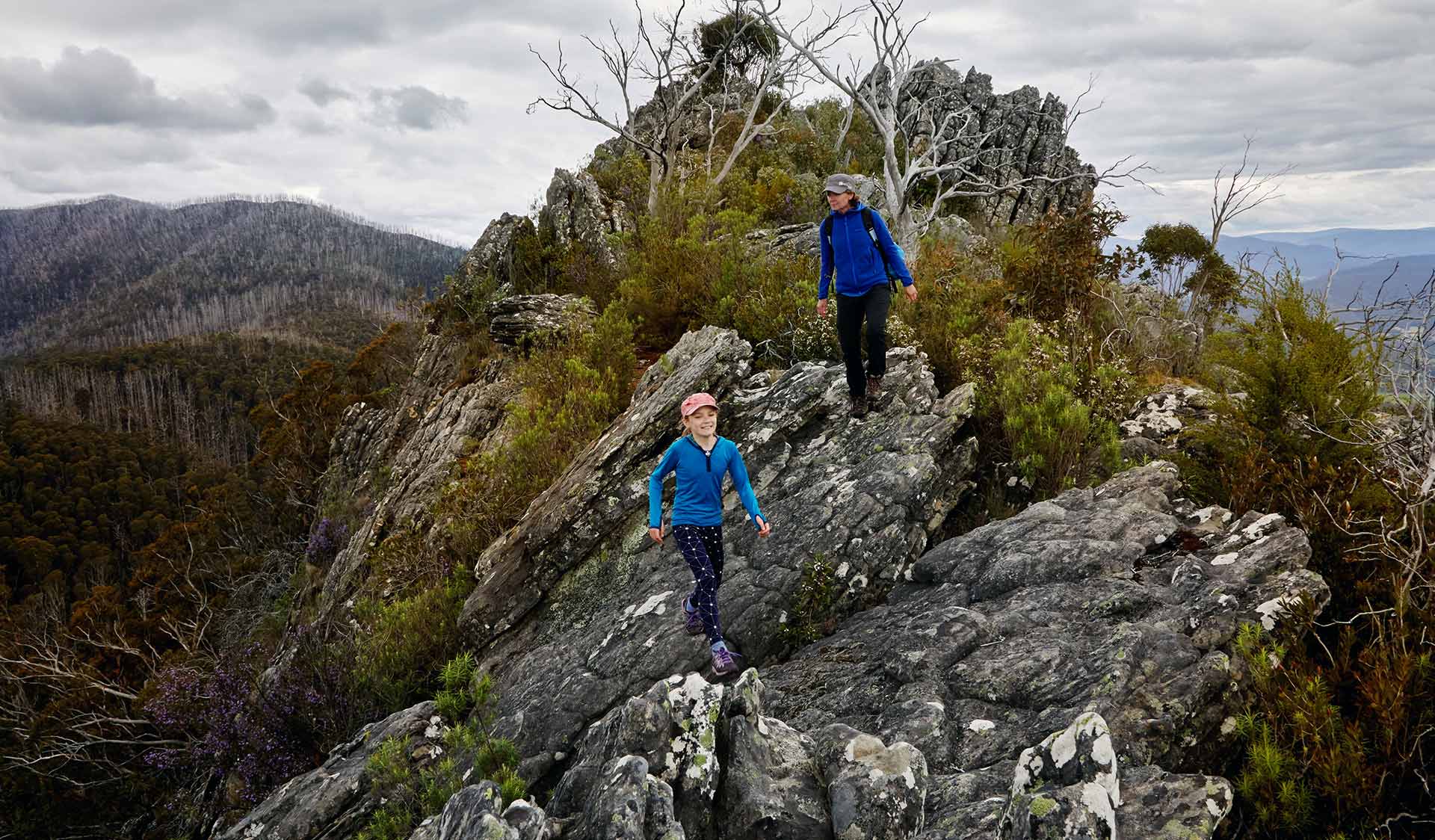 A mother and young daughter walk across Sugarloaf Saddle in magnifficent panoramic views either side of them.