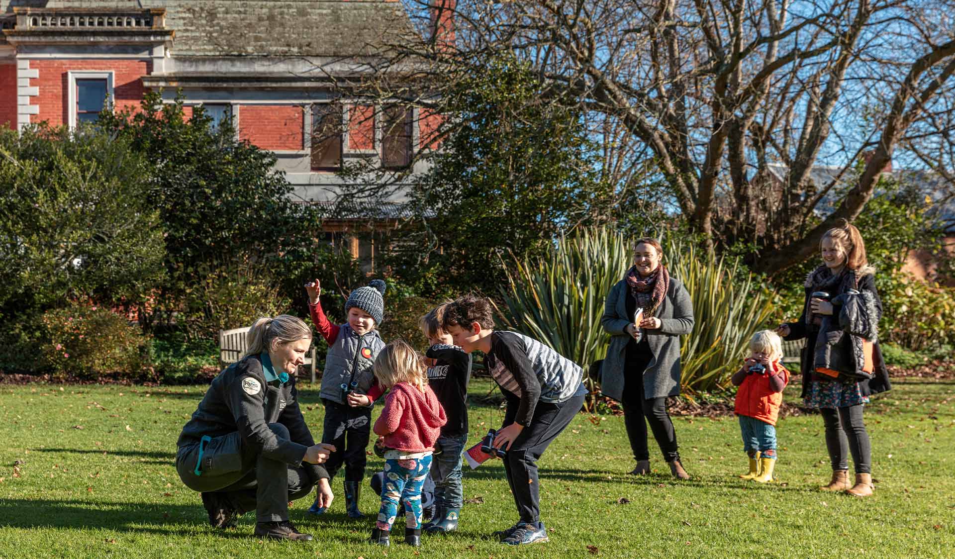 A group of children play with a ranger on lawns in front of Coolart Homestead