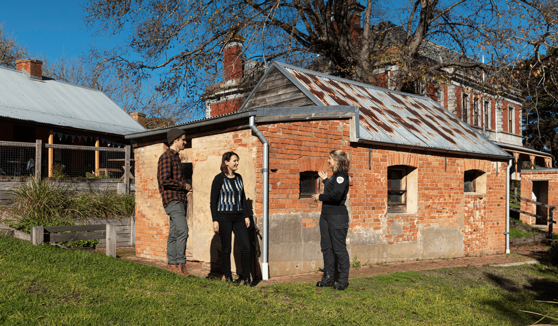 A Parks Victoria Ranger speaks to a couple outside an old building in Coolart Heritage Area
