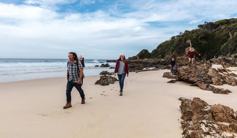 A family walk together along the water's edge at Shipwreck Creek beach.