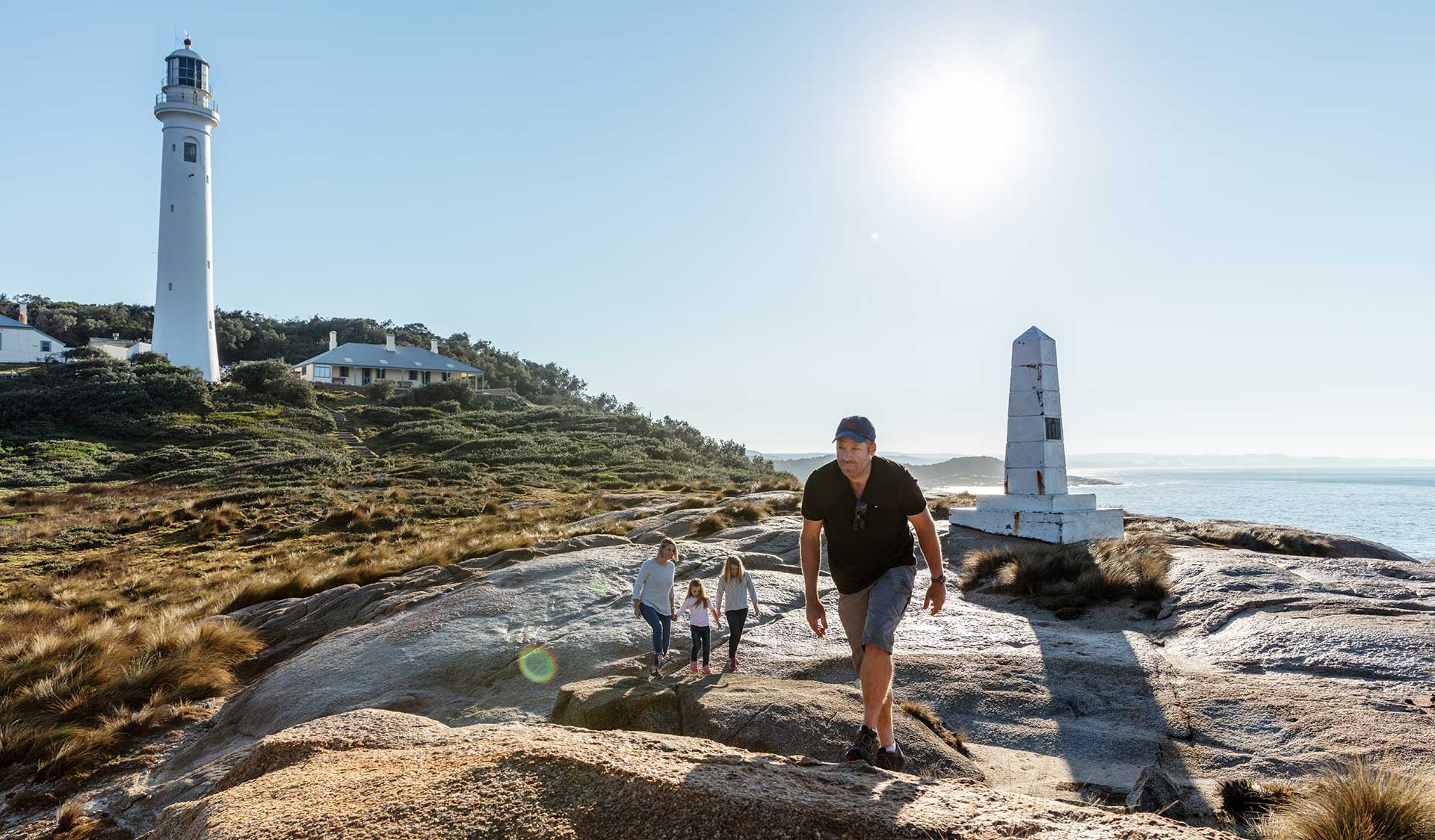 A father leads his family across the rocks in front of the Point Hicks Lighthouse and cottage.