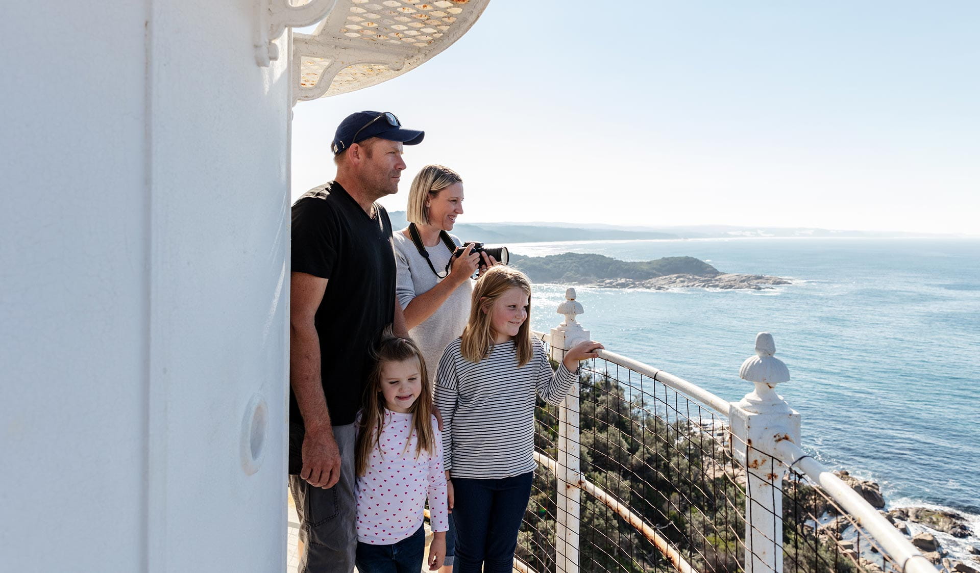 A mother, father and their two young daughts gaze out at the sea from the lookout point of the lighthouse.