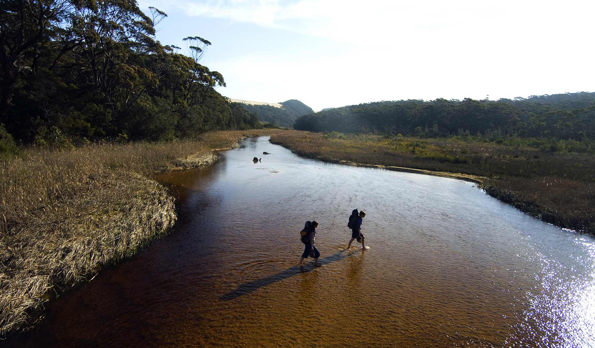 Two hikers cross an estuary in the Croajingolong National Park. 