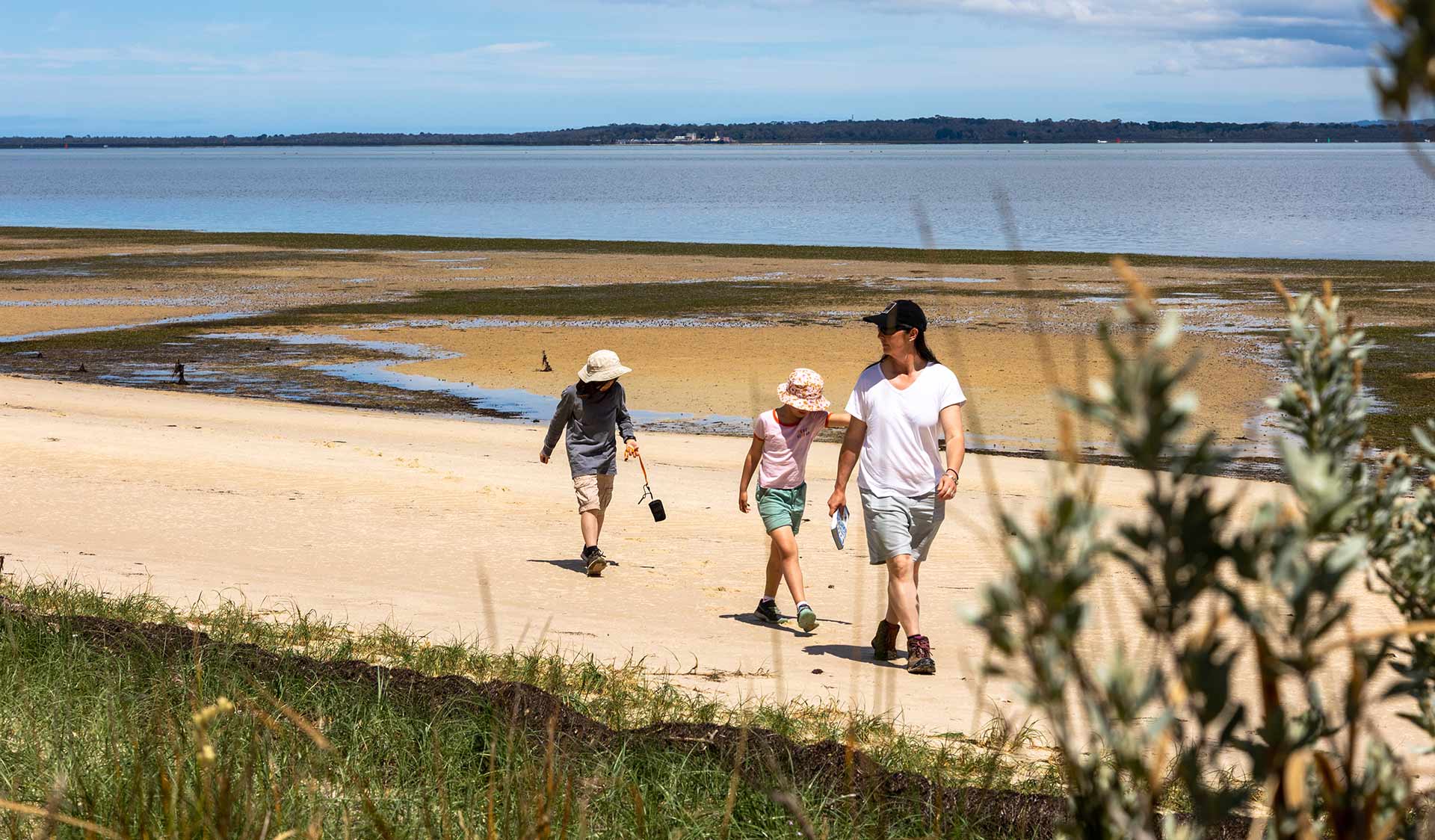 A mother and her two children walk along Fairhaven Beach with views of Western Port in the background at French Island National Park 