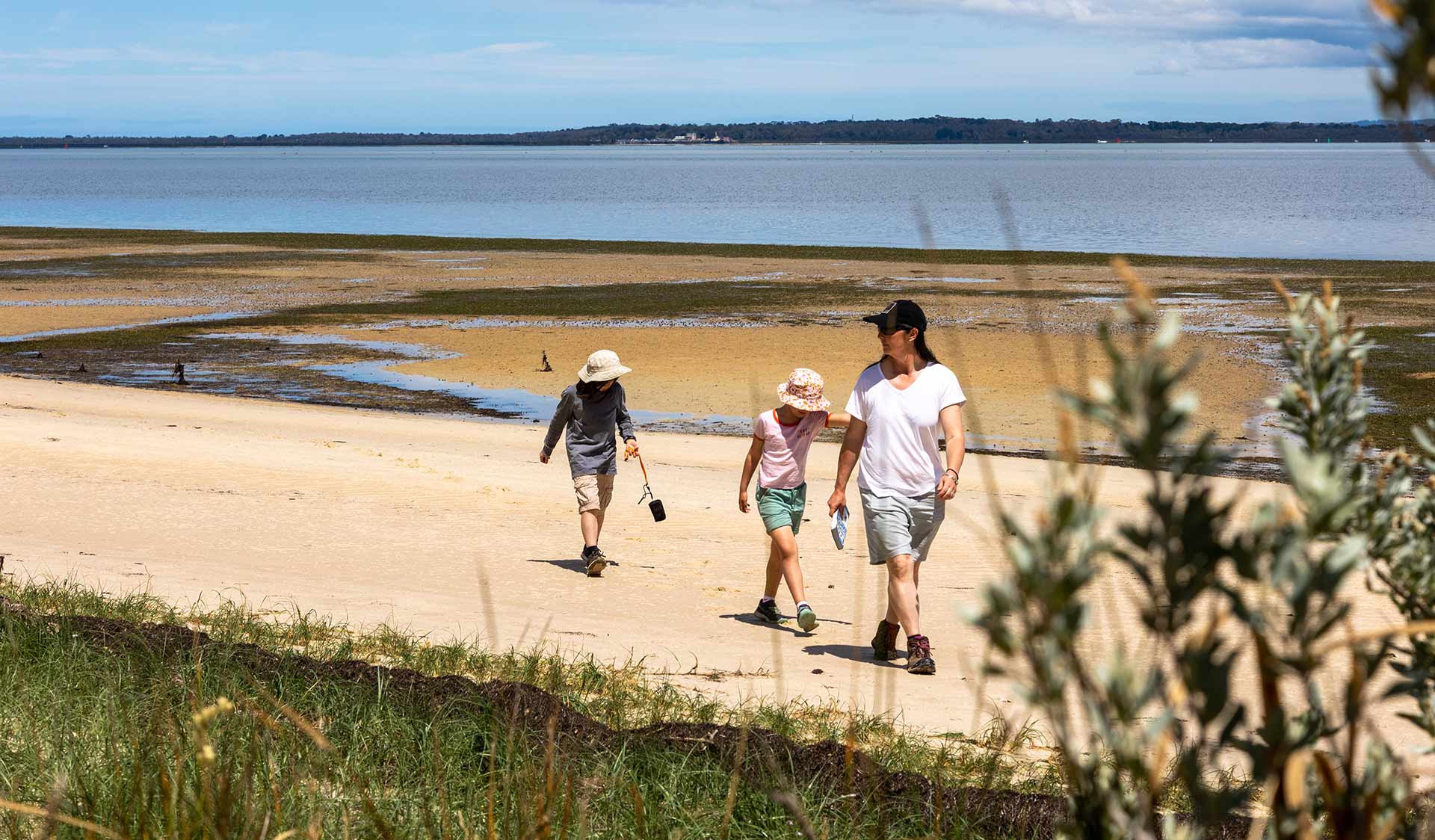 A mother and her two children walk along Fairhaven Beach with views of Western Port in the background at French Island National Park