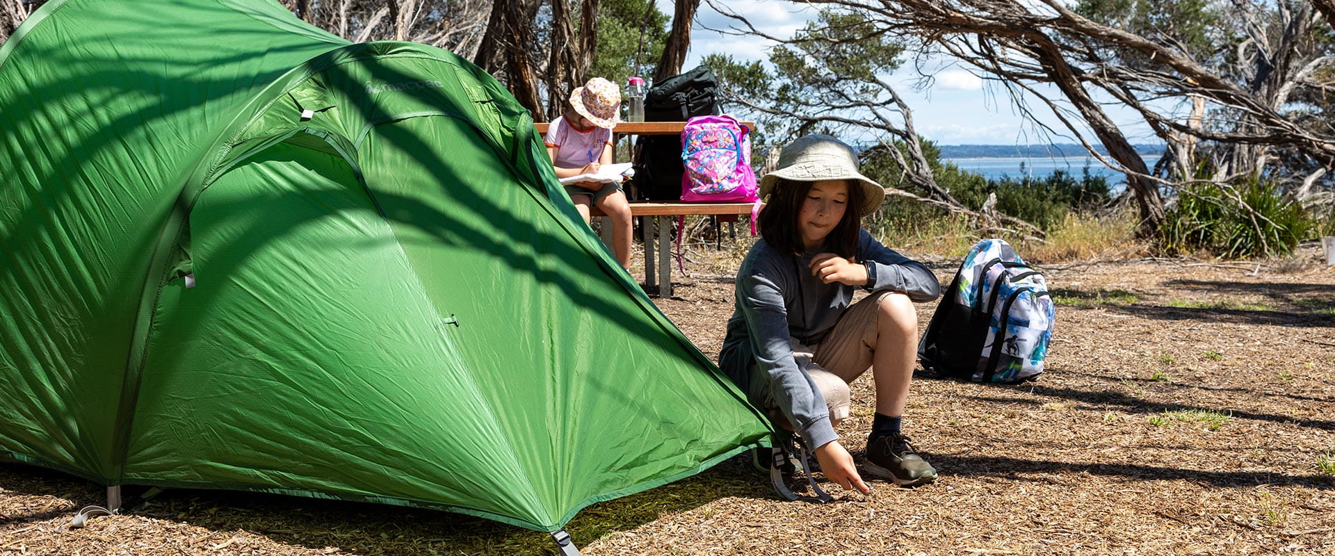 A young boy sets up tent while his sister draws in the background