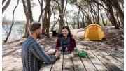 A woman enjoys a cup of tea while sat at a picnic table infront of her tent at Bunga Arm Campsite in the Gippsland Lakes.