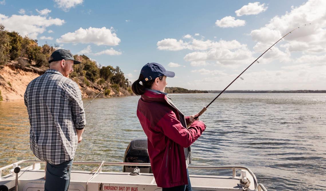 A man and a women fish off the back of a boat.