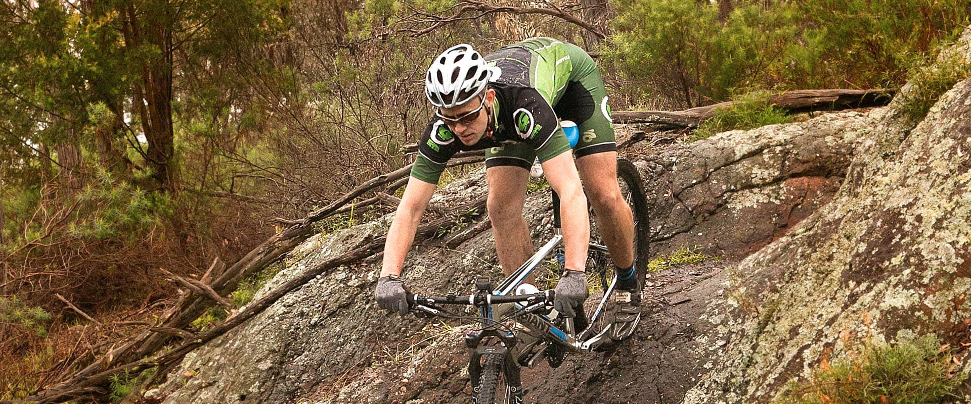 A person rides a mountain bike down a rocky outcrop in a rugged bushland.