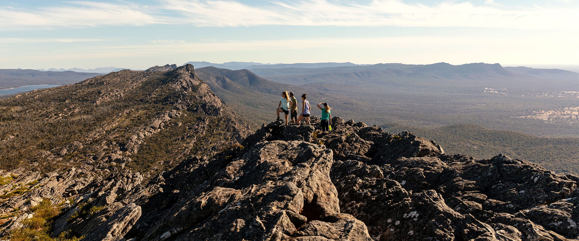 A group of hikers walk stand at the top of Gar's summit overlooking the landscape
