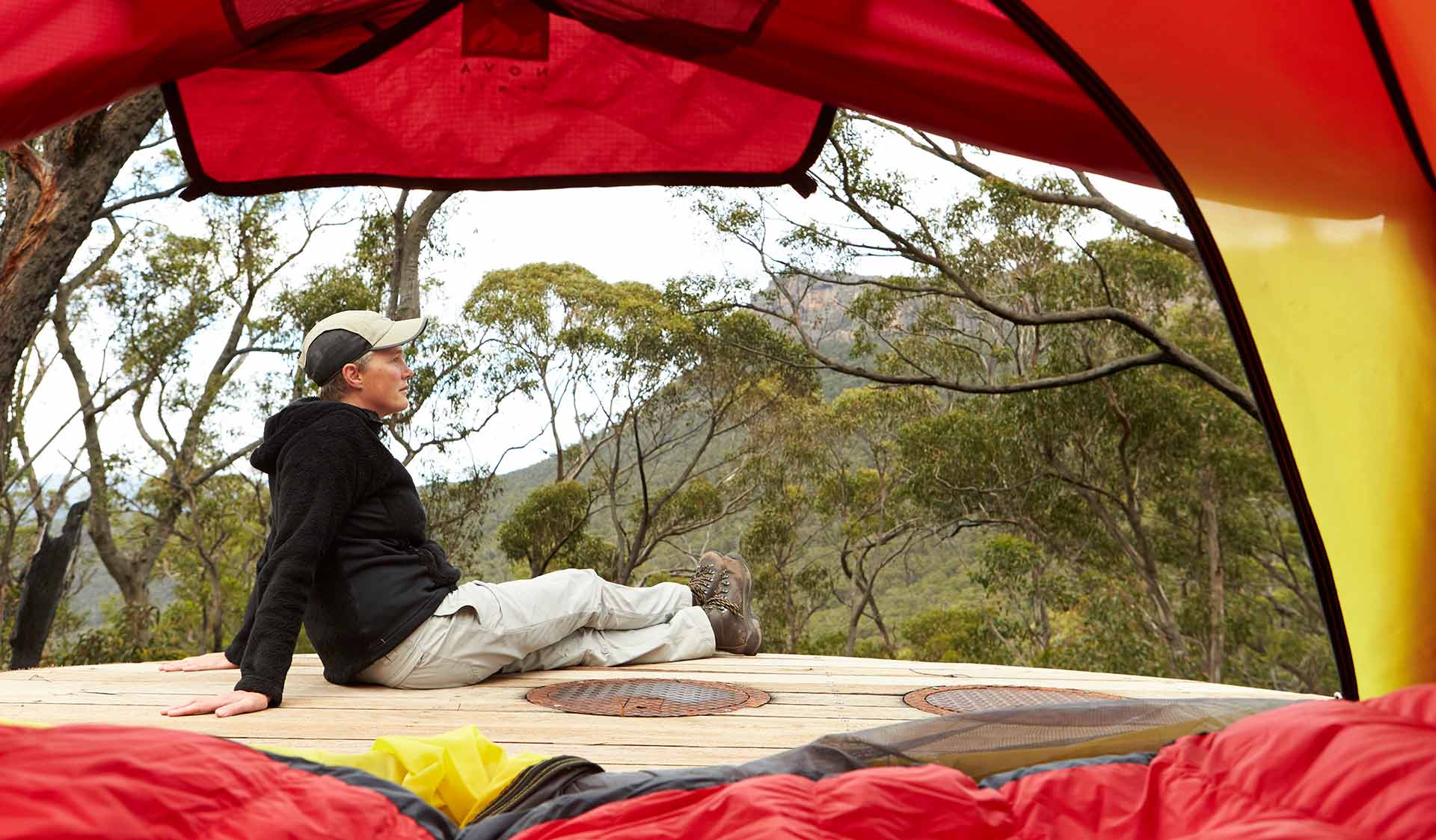 The view, from inside a tent, of a women sitting nest to a tent at Bugiga Hiker Camp on the Grampians Peaks Trail