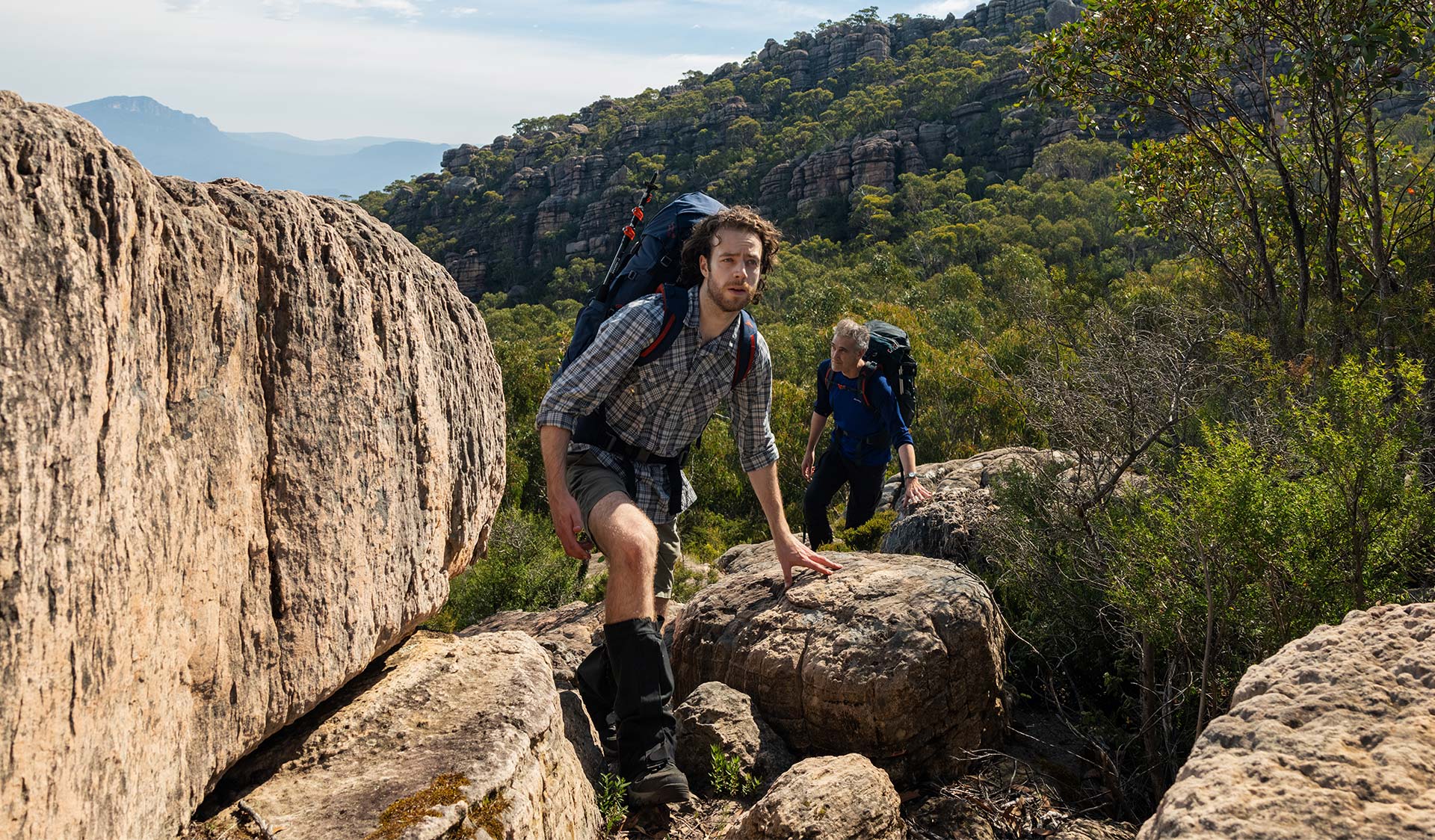Two hikers wearing hiking bags climb a rocky track