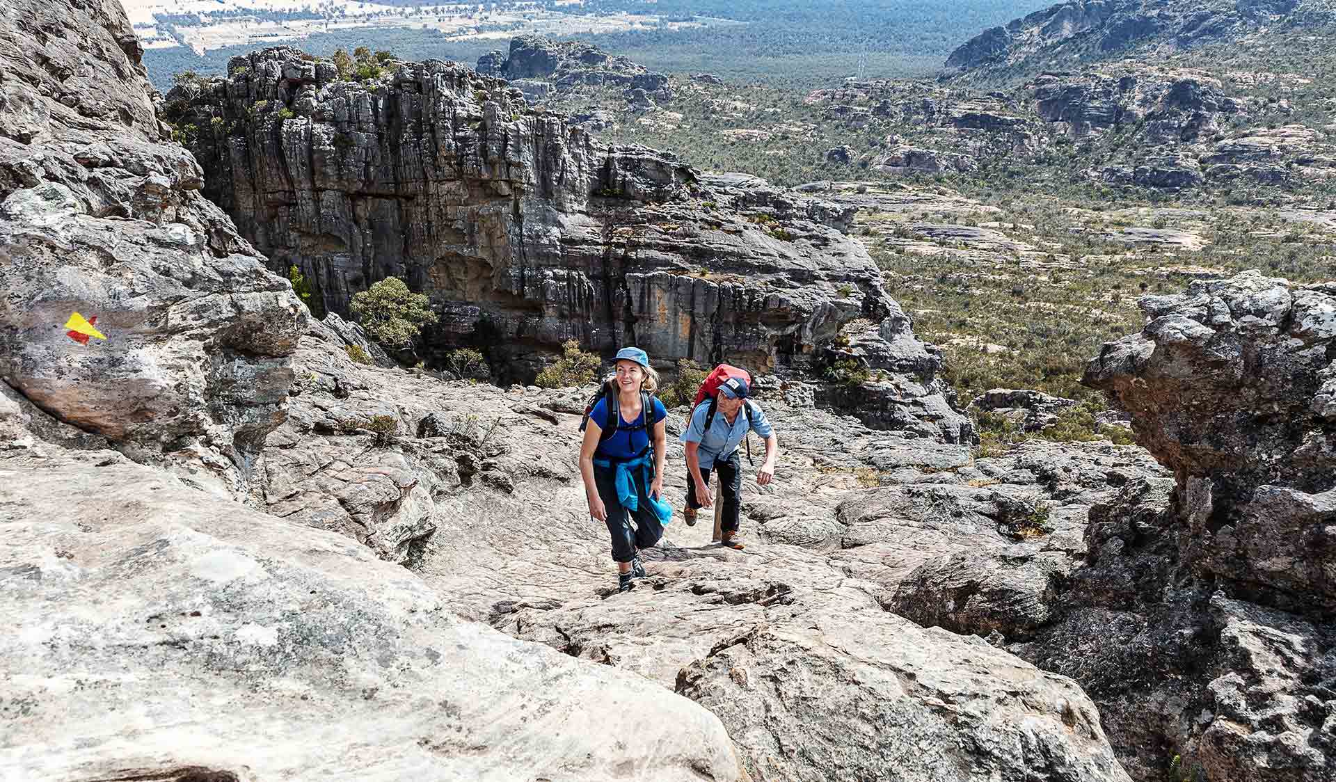 A man and woman climb up the rocky landscape of Mt Stapleton.