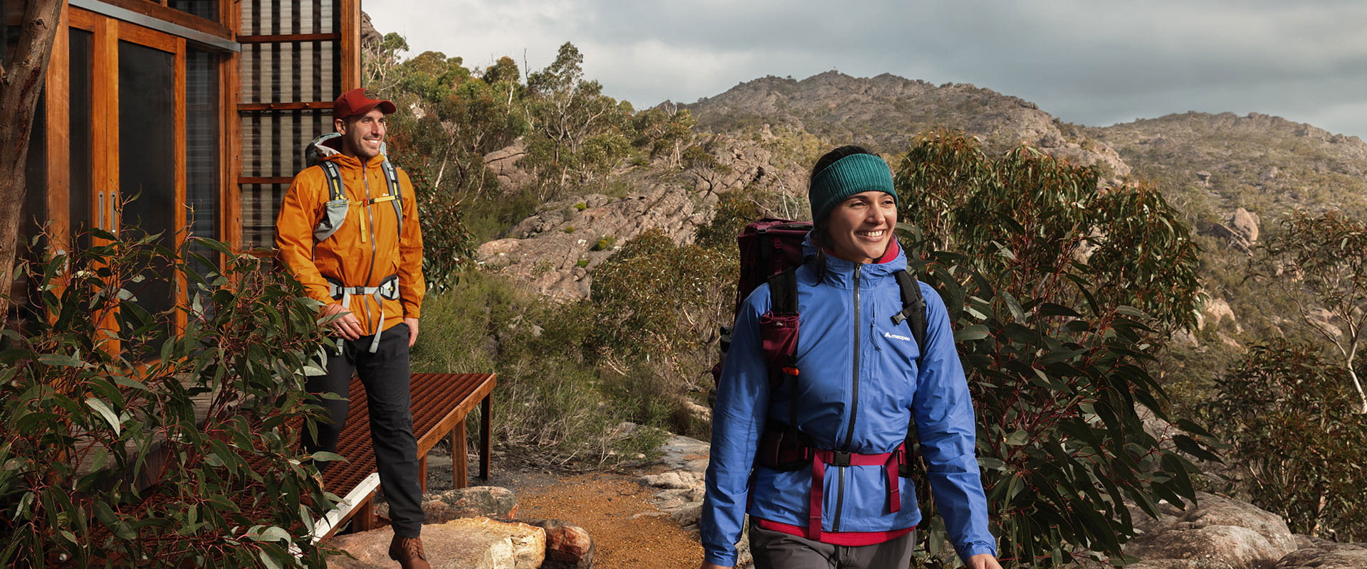Two hikers depart their cabin surrounded by mountainous views