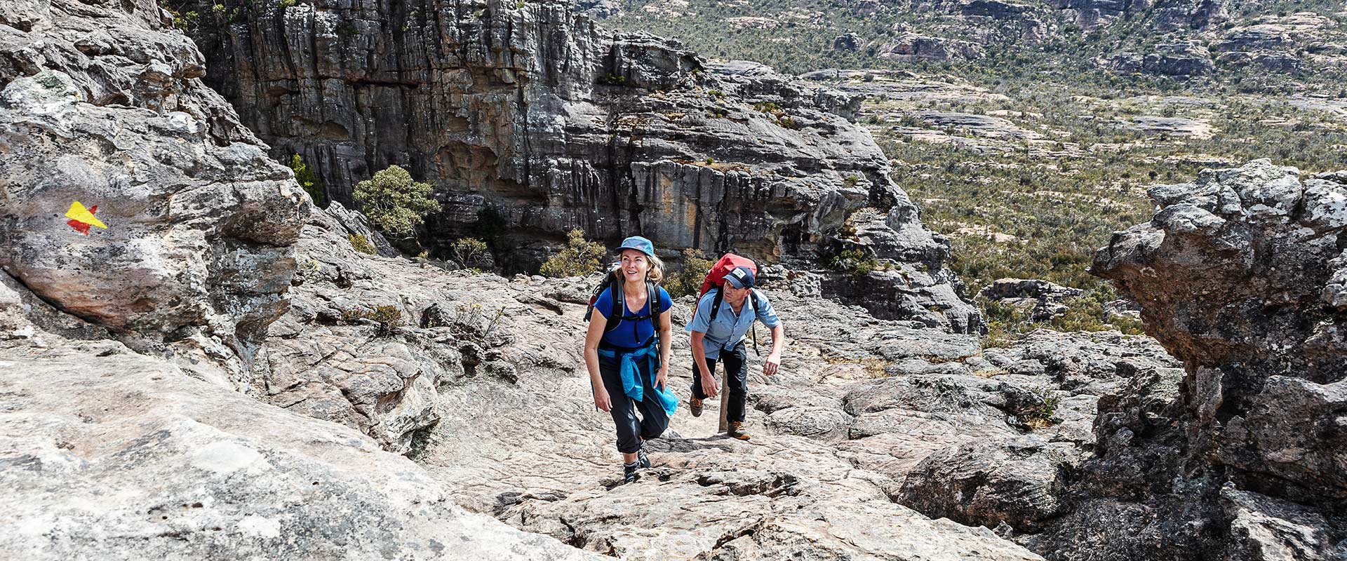 A man and woman climb up the rocky landscape of Mt Stapleton.