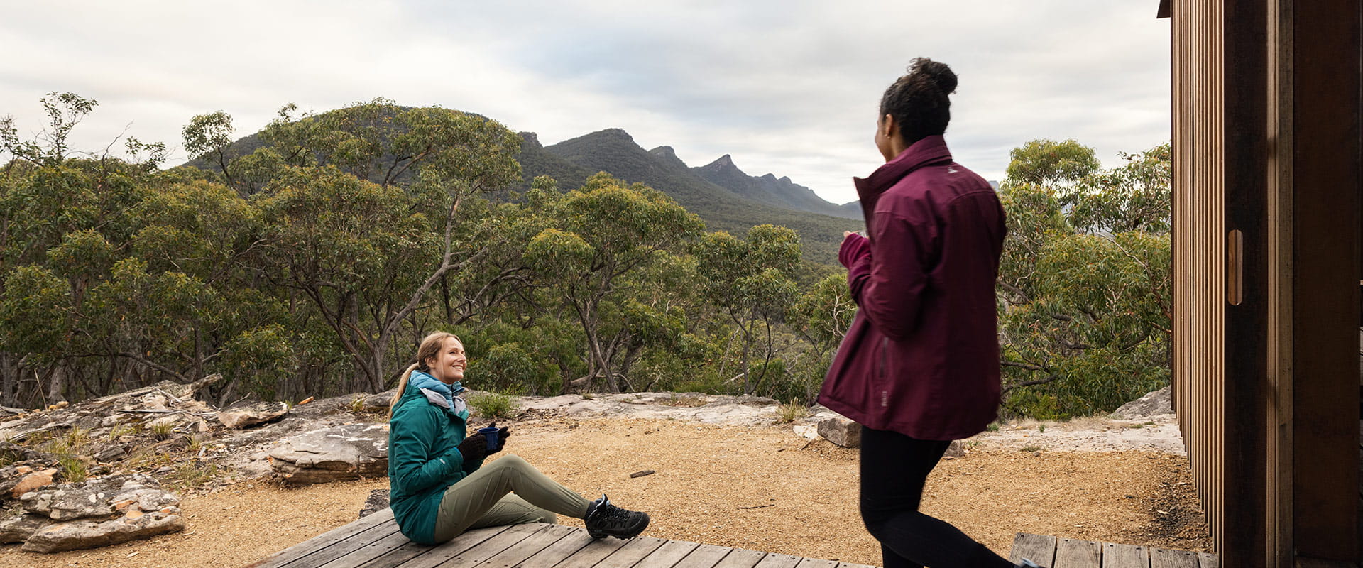 Two hikers enjoy a morning coffee on the steps of the shelter and take in the mountainous views