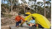 A man passes a cup of tea to his partner at their tent set up below the communal shelter at Djardji-Djawara Hiker camp on southern section 2 of the GPT