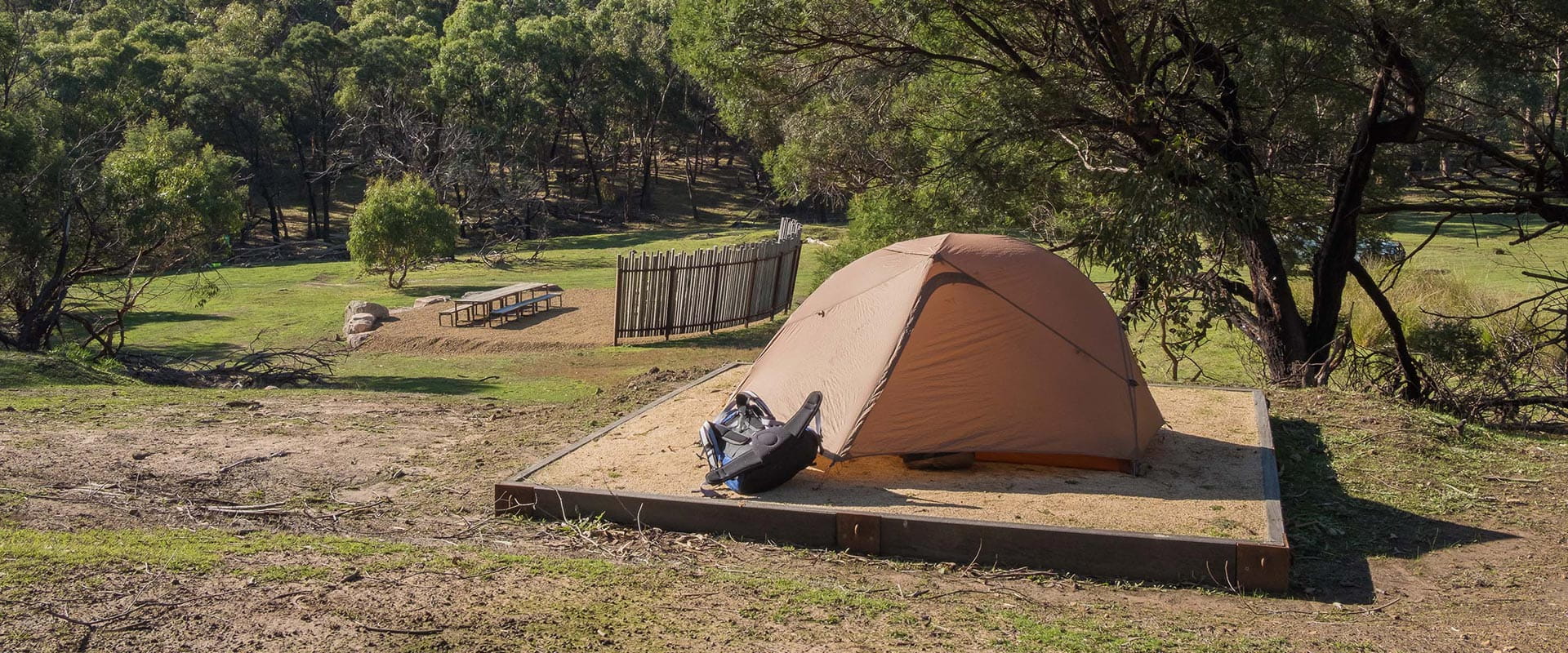 A tent sits on a hill overlooking a grassy campsite and picnic area
