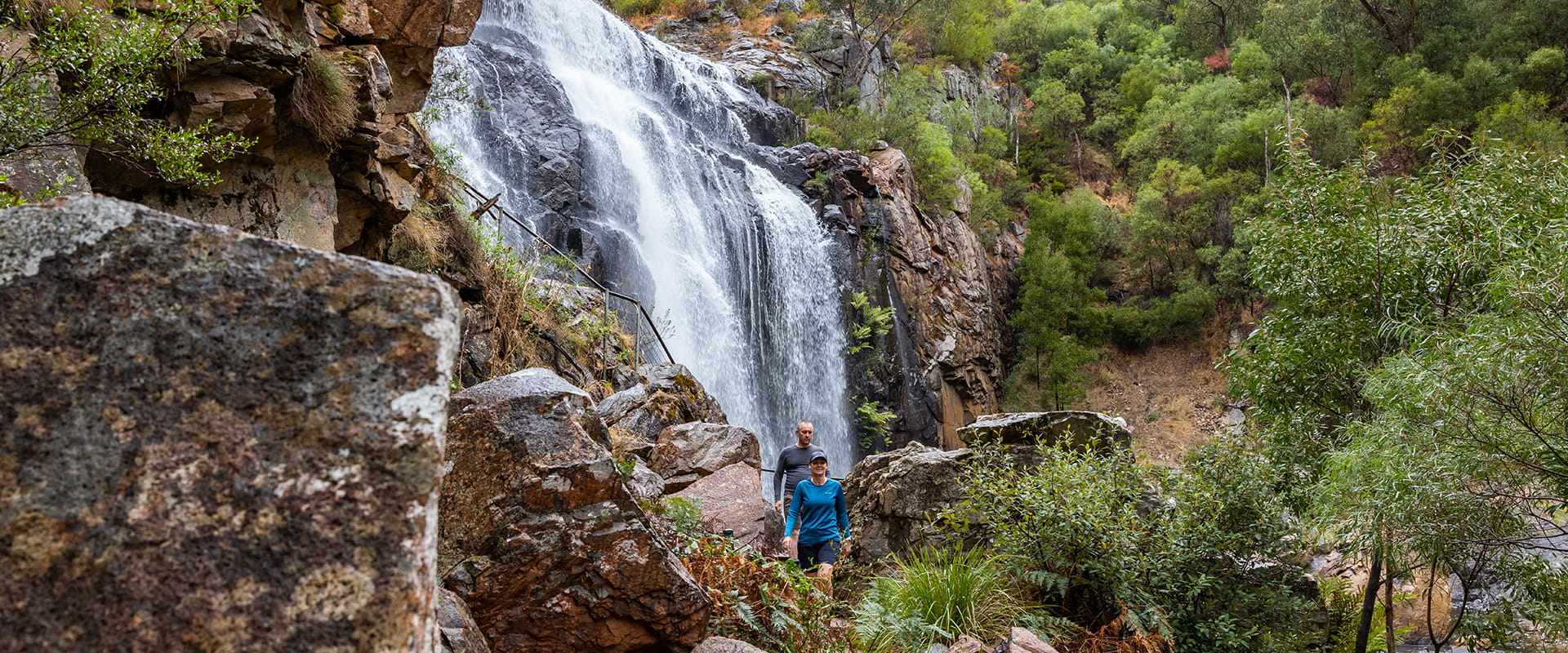Two people walking along the path in front of Mackenzie Falls at Grampians National Park