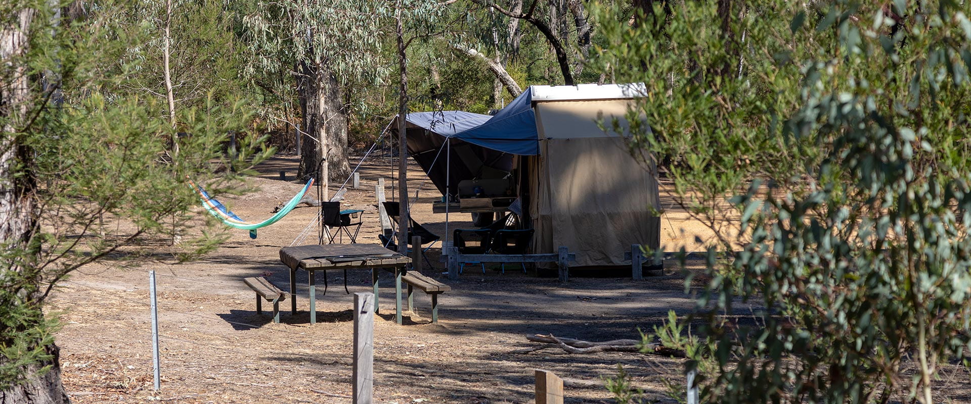 A drive in campground with a 4wd and tent set up amongst trees
