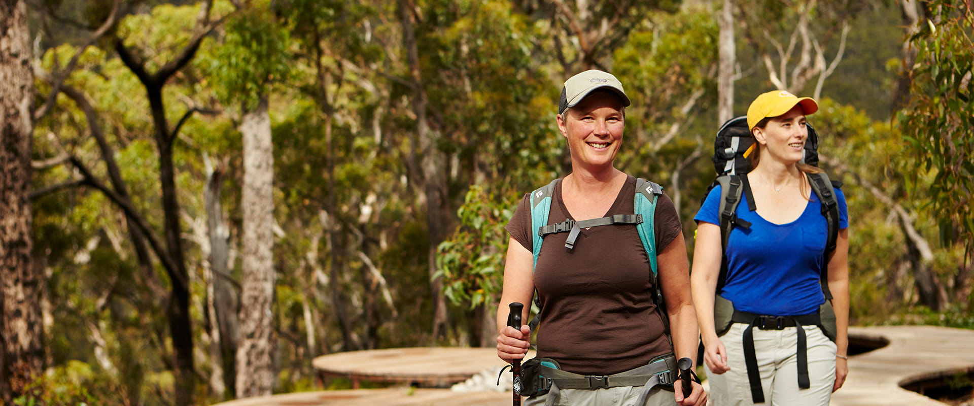 Two happy hikers arrive at a campground there are tent pads in the background and lush trees