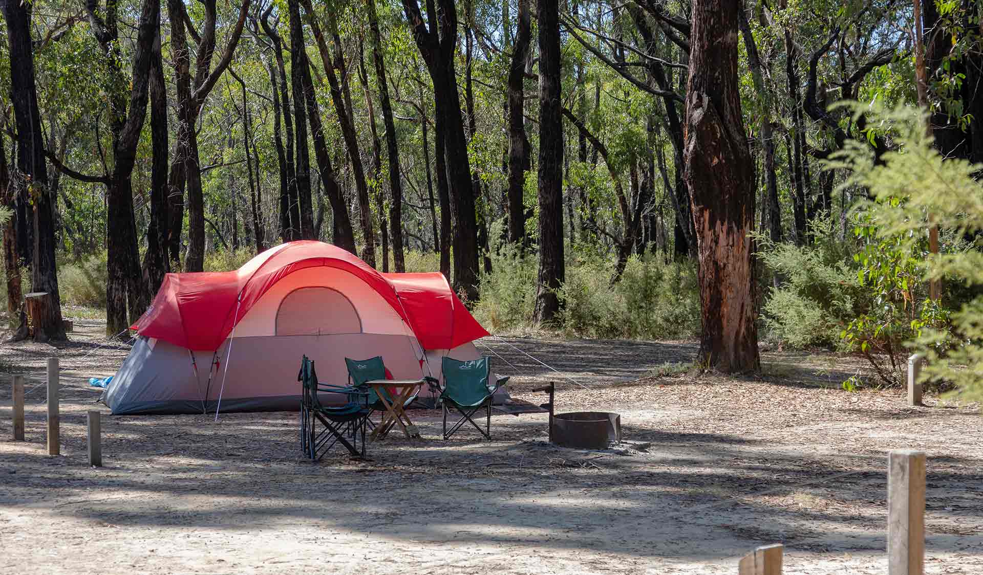 A red tent, camp chairs and fireplace among tall eucalypts at Strachans Campground at Grampians National Park