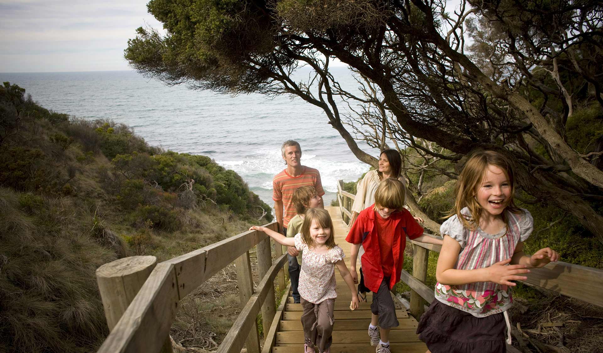 A family walks up a set of wooden stairs on the Surf Coast Walk.