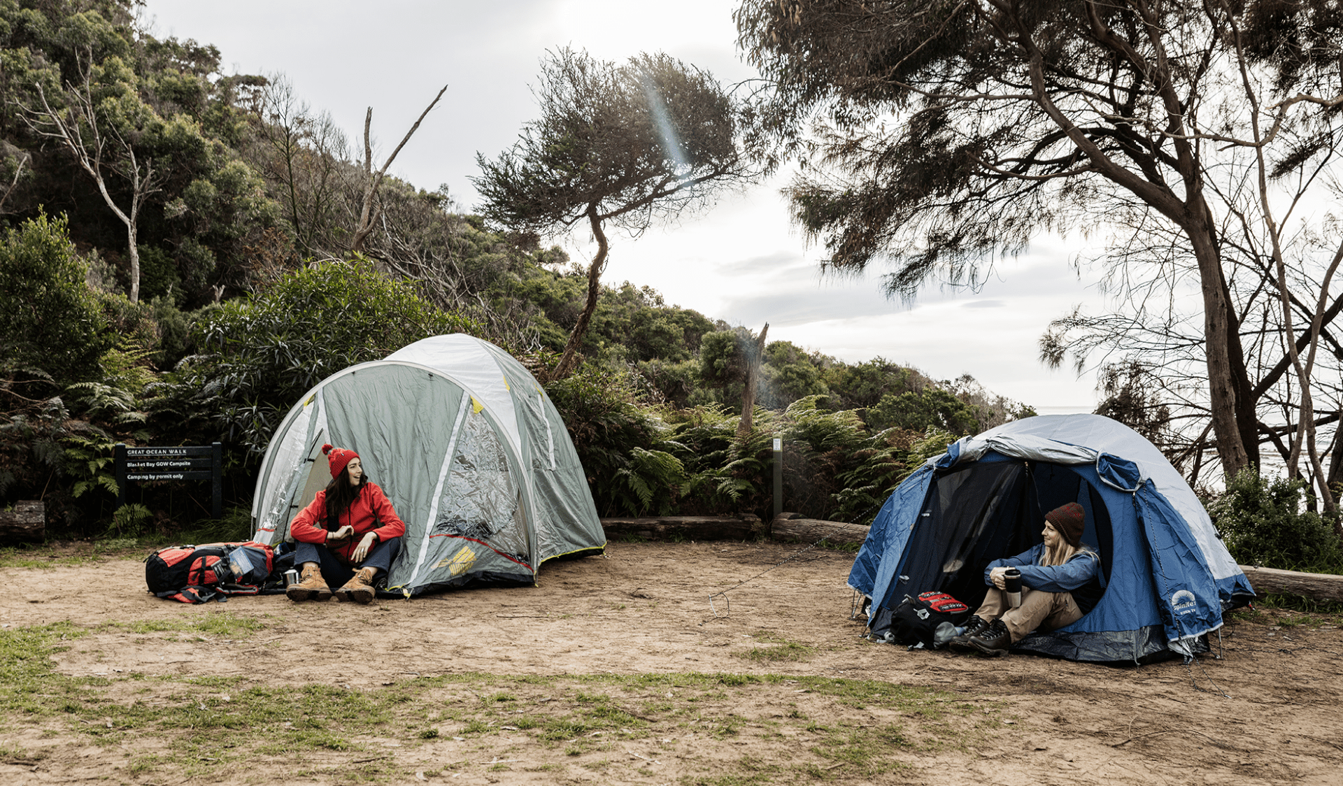 Two female hikers sit outside their tents at Blanket Bay Hike-in Campground