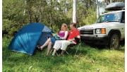 A couple sit and look at a map next to their tent and car.