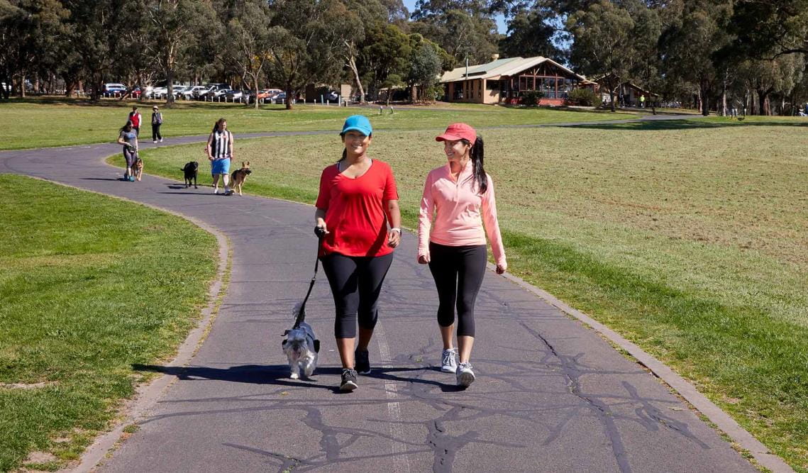 A woman and friend in activewear walking a small dog at Jells Park