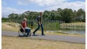 Two men, one in a wheelchair, in front a pedestrian bridge and near the water's edge at Karkarook Park 