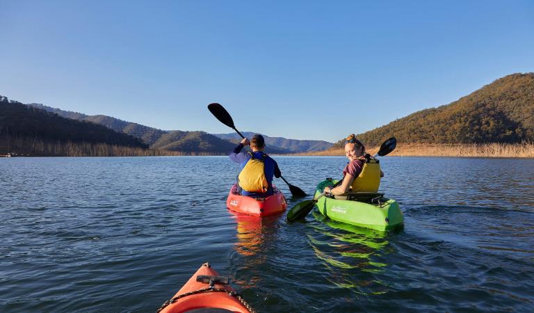 A young couple paddle kayaks on a sunny afternoon across Lake Eildon.