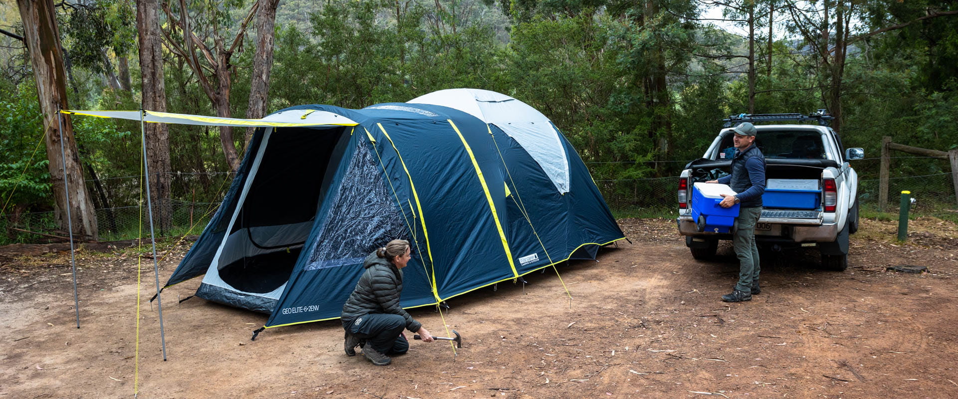 Two people pitch a tent in a bushland landscape. 