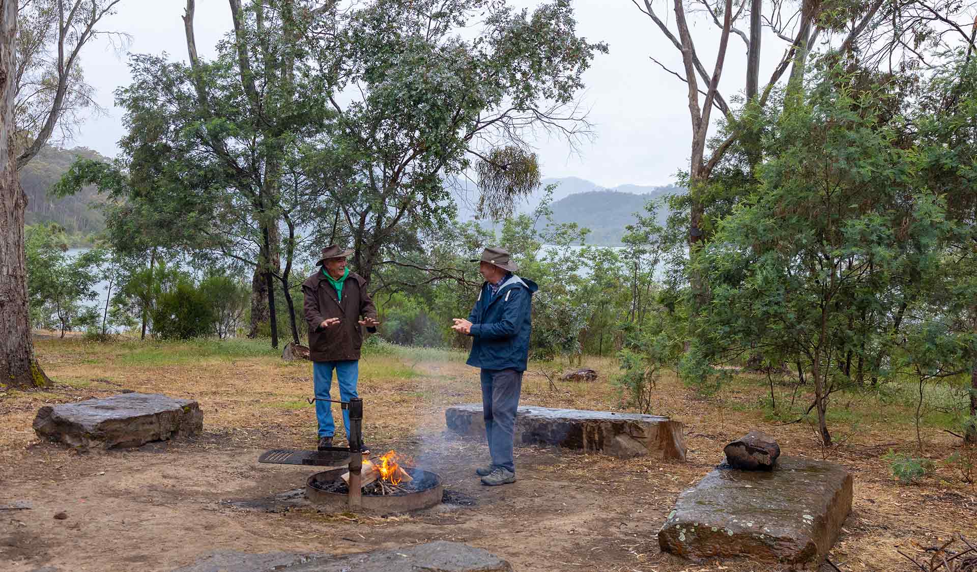 Two men warm up next to campfire at Devil Cove Campground at Lake Eildon National Park