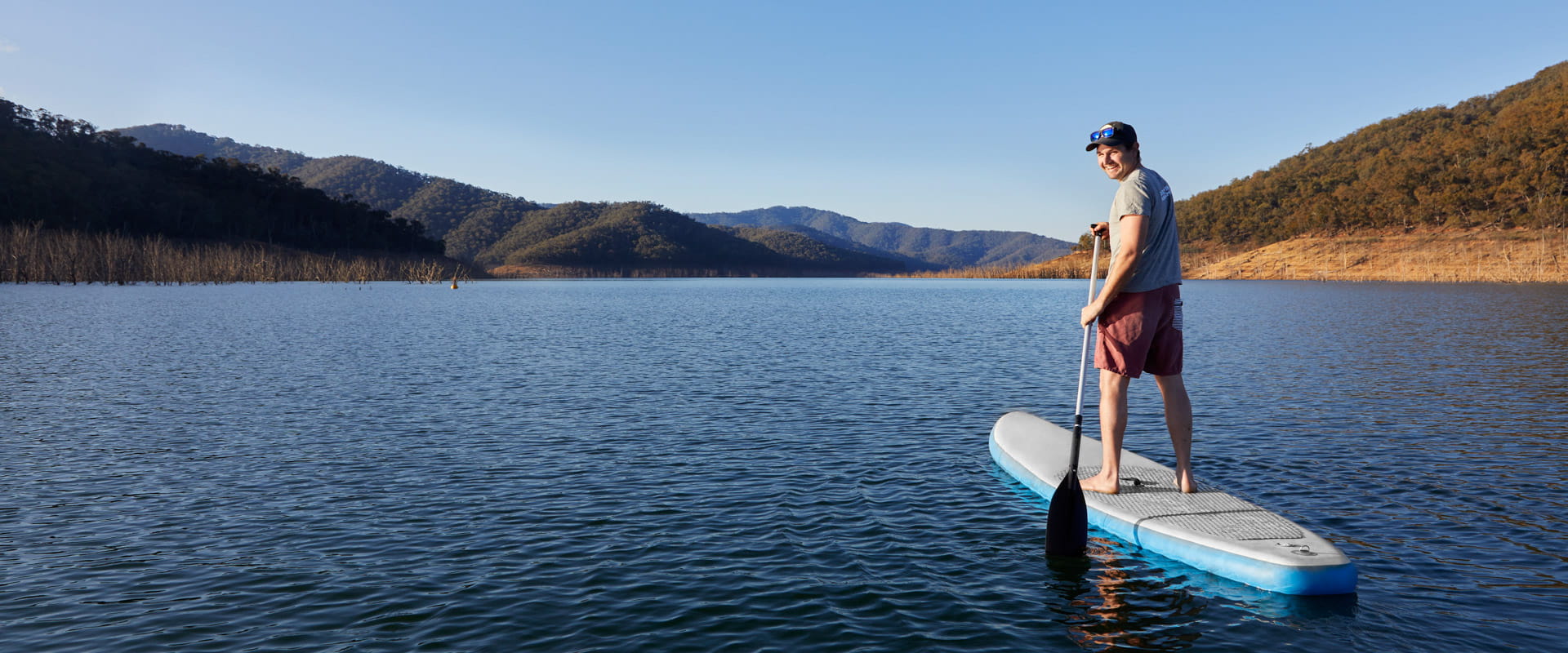 A man floats in the middle of a large blue lake on top of a stand up paddle board.